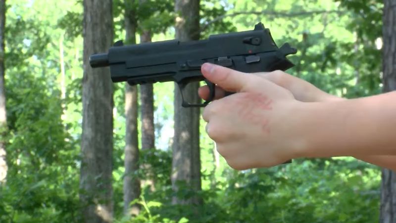 A child holding a handgun outdoors, showing a dangerous result of improper firearms storage