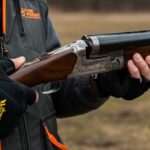 A man stands holding a shotgun in his right hand
