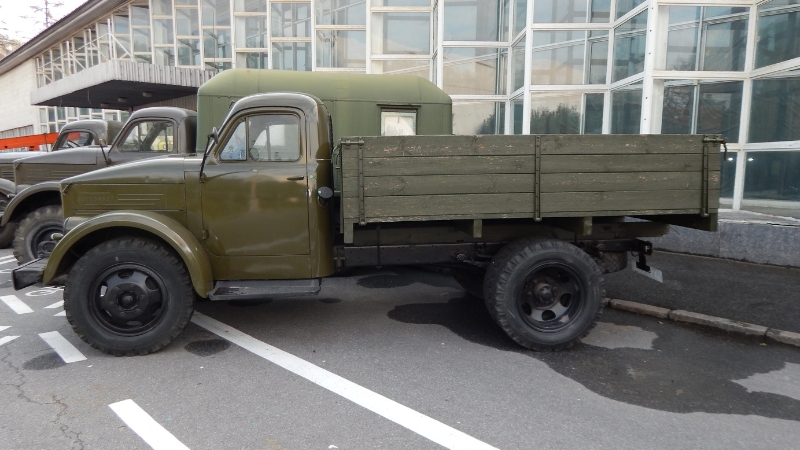 A vintage military transport truck parked outside a glass building on a marked lot