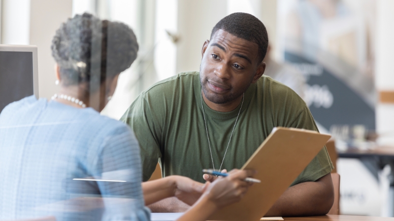 A US Army recruit speaks with a staff member while reviewing documents during an identity and legal presence check