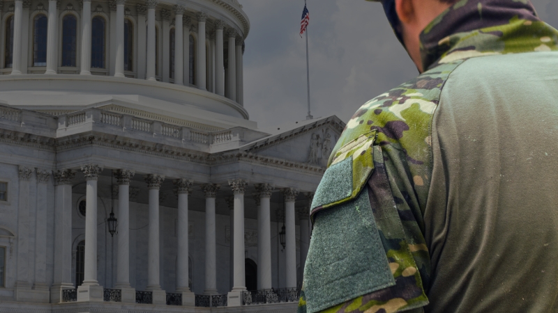 A soldier in camouflage stands near the U.S. Capitol building with an American flag in the background
