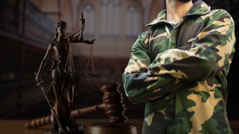 A soldier in camouflage stands beside a Lady Justice statue and gavel, symbolizing legal challenges in military entry