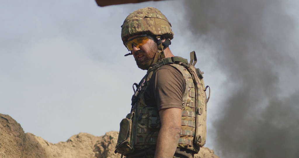 Soldier in camouflage gear and helmet with smoke in the background, representing readiness and survival skills in uncertain environments