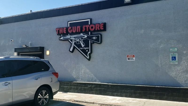 A gun shop in Las Vegas with a large wall sign reading โThe Gun Storeโ beside a parked silver SUV