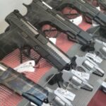 Handguns displayed in a gun shop showcase, each tagged with price labels