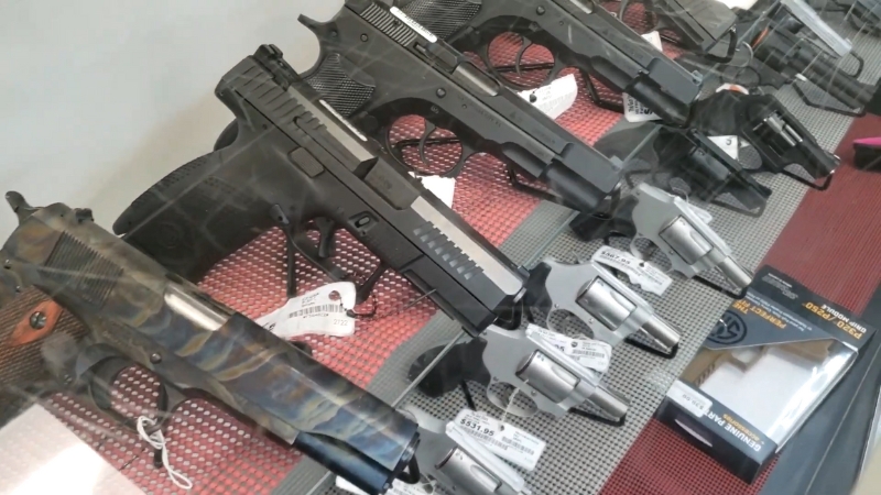 Handguns displayed in a gun shop showcase, each tagged with price labels